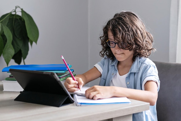 Menino de escola adorável com óculos estudando on-line de criança em casa usando tablet digital