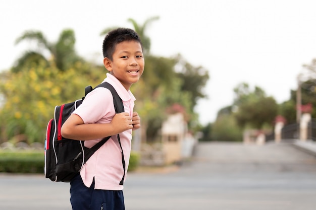 Menino de escola asiático feliz no uniforme com trouxa que anda para trás em casa.