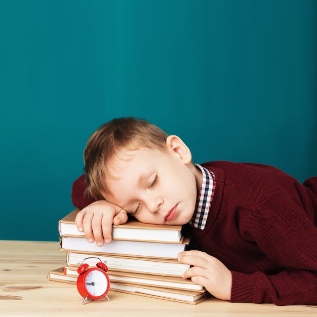 Menino de escola cansado dormindo em livros. pequeno estudante dormindo em livros didáticos