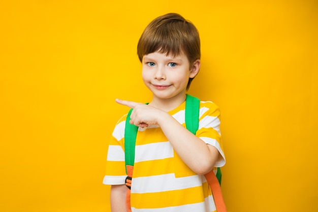 Menino de escola elegante com o dedo apontando em fundo amarelo