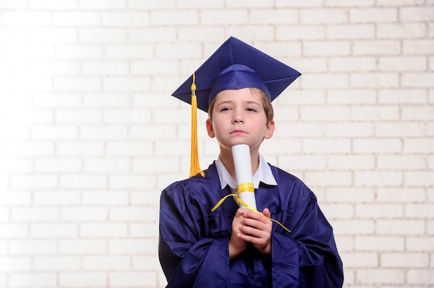 Menino de escola vestido de formatura aponta para cima com o dedo.