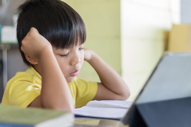 Foto menino de estudante asiático usando e tocando o teclado inteligente ou tablet para fazer sua lição de casa