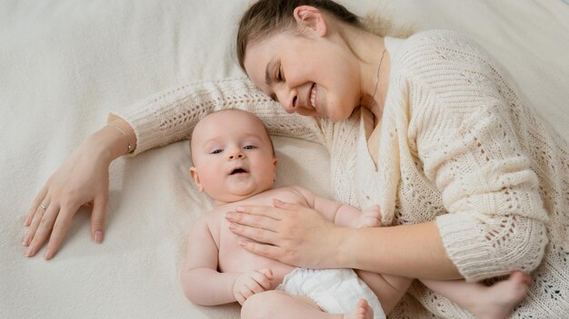 Foto menino de fraldas deitado ao lado da mãe na cama conceito de cuidar do bebê e da família