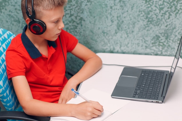 Menino de jovem estudante usando fones de ouvido com laptop, aprendendo e se preparando para voltar às aulas. conceito de educação online.