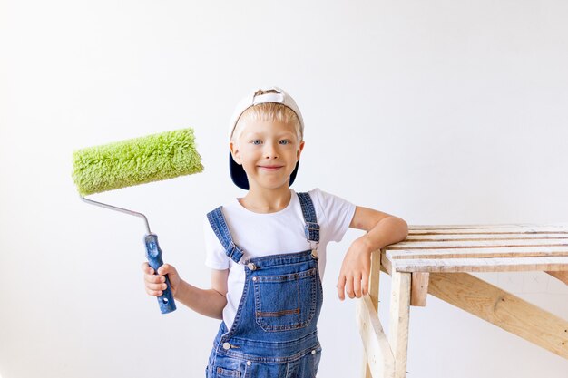 Menino de macacão segurando um rolo de pintura