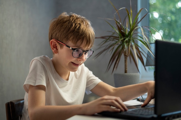 Menino de óculos joga jogos de computador com entusiasmo. Jogador infantil. Problemas da juventude moderna.