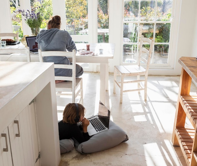 Foto menino de oito anos deitado no queixo de almofadas nas mãos assistindo uma tela de laptop fazendo lição de casa