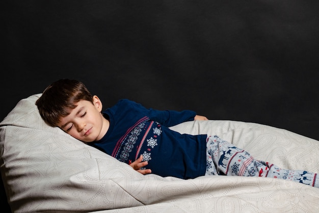 Foto menino de pijama em um fundo preto dormindo