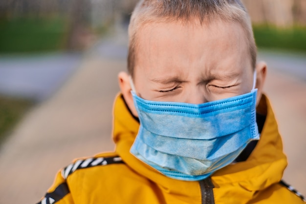 Menino de seis anos usando uma máscara médica em uma rua na primavera