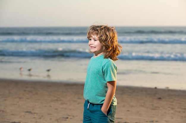 Menino de tshirt com a mão no bolso andando na praia de verão