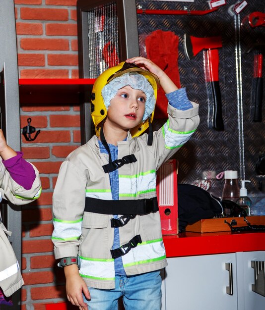 Foto menino de uniforme de bombeiro em frente à parede do corpo de bombeiros