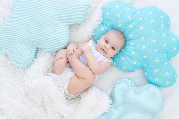 Menino deitado na cama antes de ir para a cama, lindo, rindo, bebezinho sorridente de seis meses