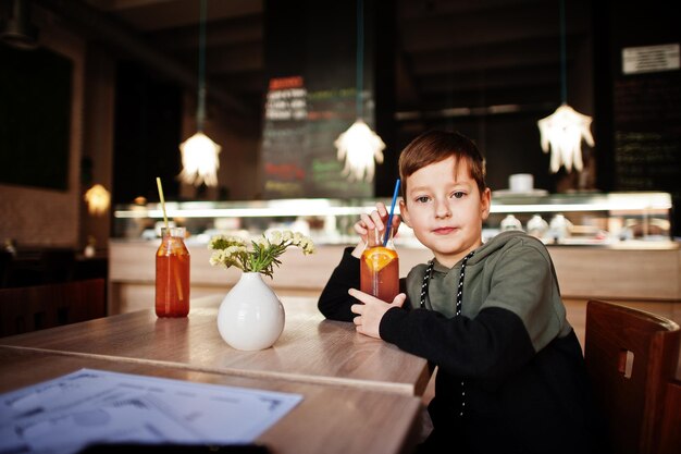 Menino descansa depois da escola sentar no café e beber coquetel de suco