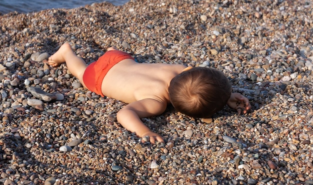 Menino descansando deitado sobre as pedras na praia rochosa no mar Mediterrâneo
