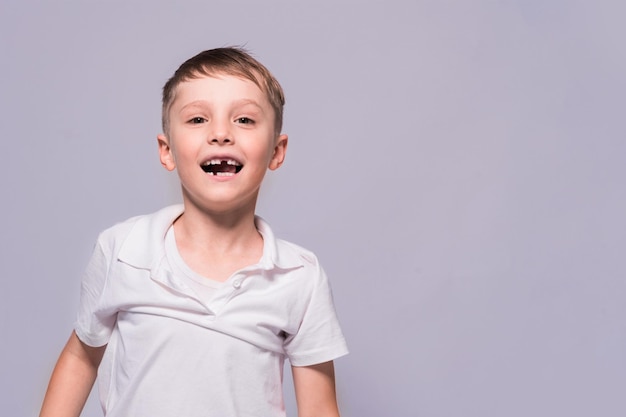 Menino desdentado em uma camiseta branca está sorrindo posando no estúdio