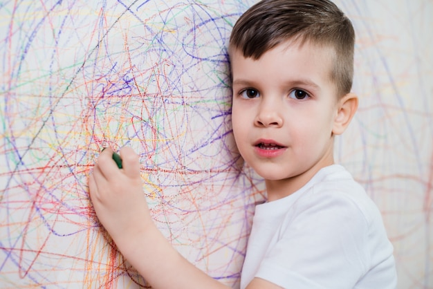 Menino desenha na parede com giz colorido. A criança está envolvida na criatividade em casa