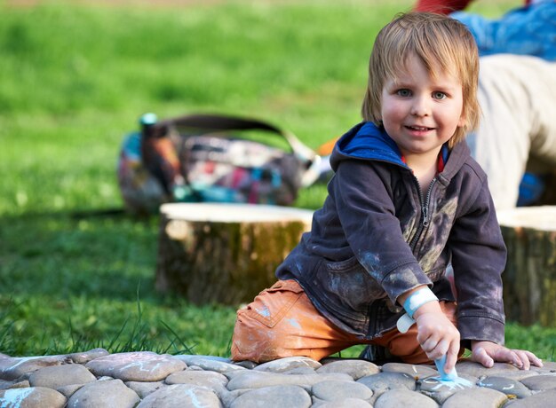 Menino desenhando com giz de calçada no parque.