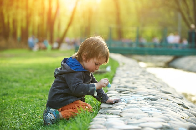 Menino desenhando com giz de calçada no parque.