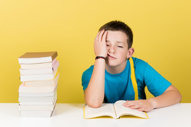 Menino desmotivado lendo livro isolado em fundo amarelo