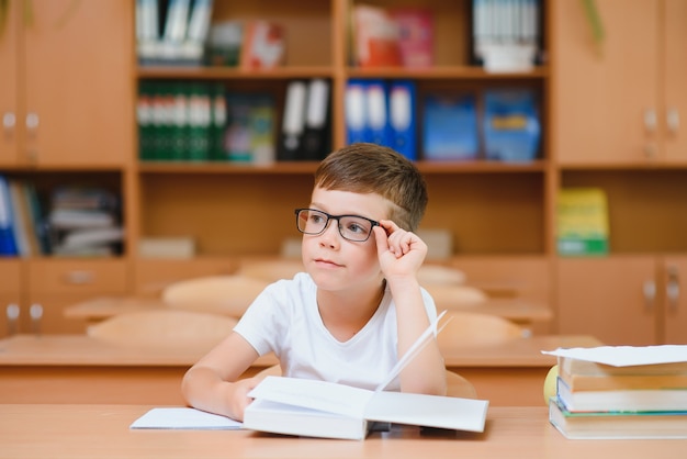 Menino do ensino fundamental na mesa da sala de aula, tentando encontrar novas ideias para o trabalho escolar.