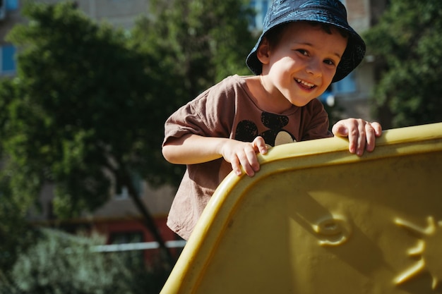 menino do jardim de infância joga em um slide no playground no verão na rua