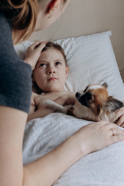 Menino doente com termômetro deitado na cama e a mão da mãe medindo a temperatura da mãe verificando a temperatura