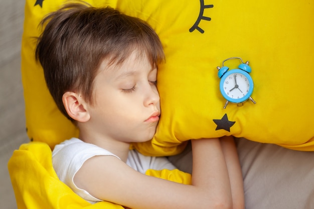 Foto menino dormindo na cama com um despertador perto de sua cabeça