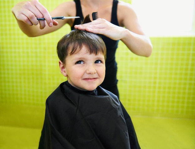 Menino e cabeleireiro com corte de cabelo no salão para penteado e grimaça com tesoura e pente Barbeiro pessoa e menino para tratamento de cabelo cuidado de cabelo e penteado com corte e feliz