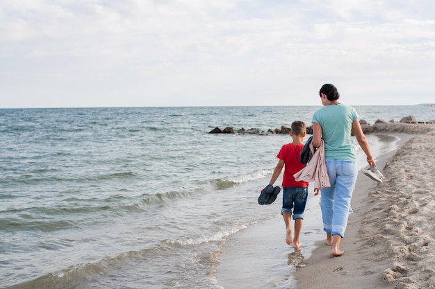 Menino e mãe caminhando na praia do mar