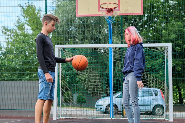 Menino e menina adolescentes jogando basquete de rua juntos, jovens com penteados da moda, jogando ao ar livre. Estilo de vida ativo e saudável, hobbies e lazer, conceito de adolescentes