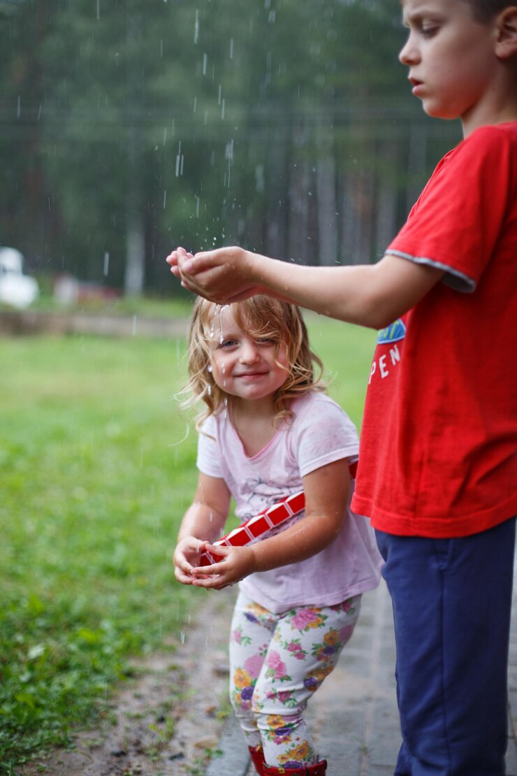 Menino e menina brincam no parque chuvoso de verão Crianças pulam em poças d'água e lama na chuva