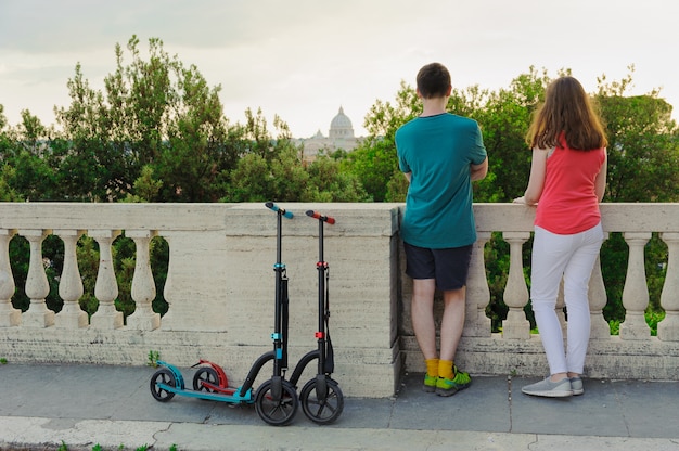 Menino e menina com suas scooters contra o vaticano no parque villa borghese.