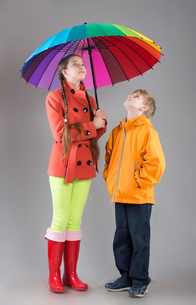 Menino e menina com um guarda-chuva colorido olhando para cima tiro de estúdio