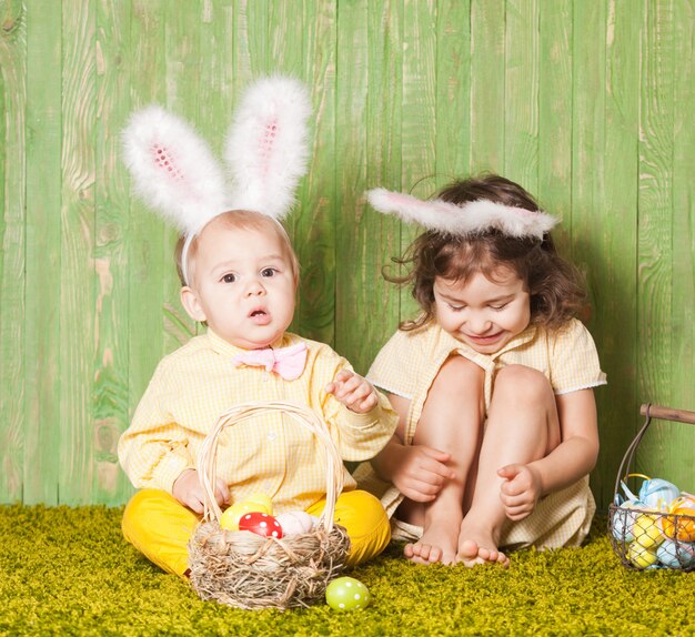 Menino e menina como coelhos da páscoa na grama com ovos coloridos