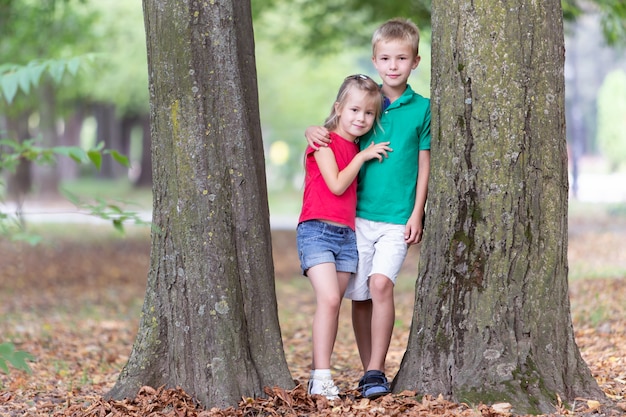 menino e menina em pé perto de tronco de árvore grande