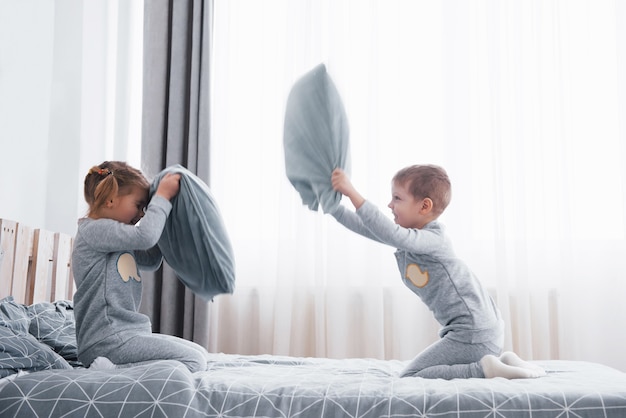 Menino e menina encenaram uma luta de travesseiros na cama do quarto. Crianças travessas batem nos travesseiros. Eles gostam desse tipo de jogo.