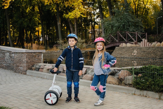Menino e menina felizes de pé e passeio no parque em Segways e scooters durante o pôr do sol. Infância feliz.