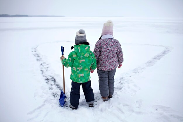 Menino e menina se divertem removendo a neve do gelo no lago congelado em forma de coração