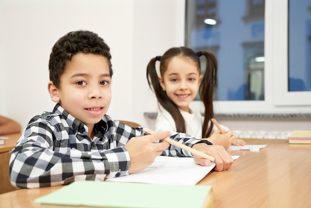 Menino e menina sentada na mesa na sala de aula, posando.