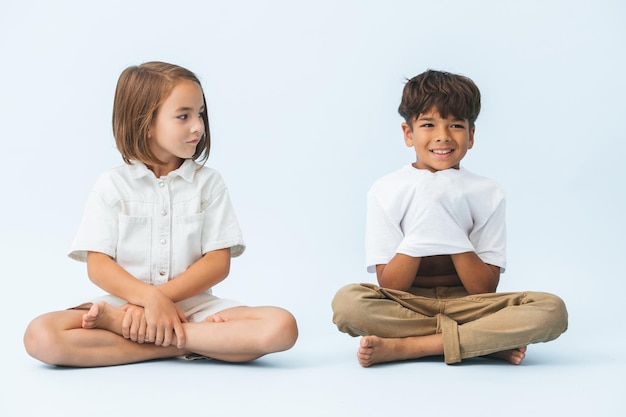 Menino e menina sentados no chão de pernas cruzadas ela olha para ele