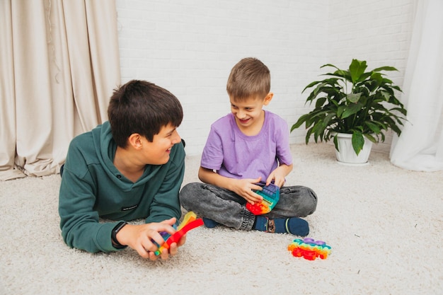 Menino e menina sentados no chão e brincando com brinquedo de silicone, anti-stress. Pop é um brinquedo sensorial. Aliviar estresse.