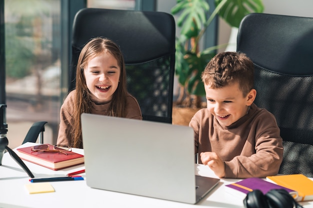 Menino e menina sorridentes estudam online em casa no laptop