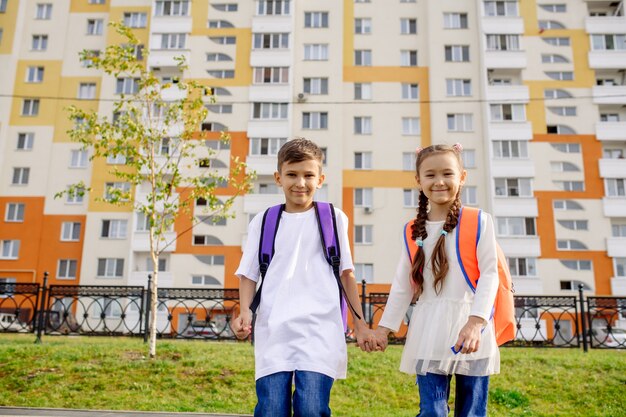 Menino e menina vão para a escola pela mão no fundo da fachada do novo prédio