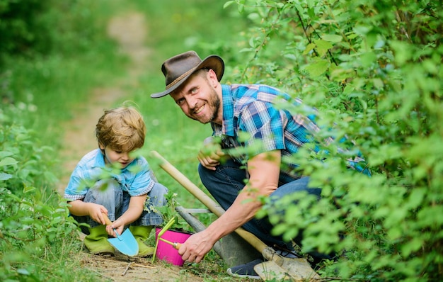 Menino e pai no fundo da natureza Ferramentas de jardinagem Passatempo de jardinagem Pai ensinando plantas de cuidado de filho pequeno Rotina de jardinagem de primavera Plantando flores Pequeno ajudante no jardim Família de fazenda