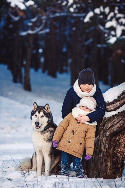 Menino e uma menina alegres com seu cachorro grande no inverno perto de uma árvore torta na floresta