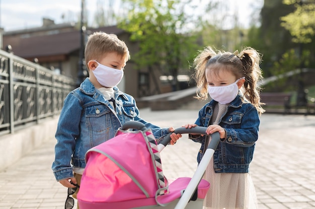 Menino e uma menina andam com um carrinho de bebê em máscaras protetoras conceito de família coronavirus covid19