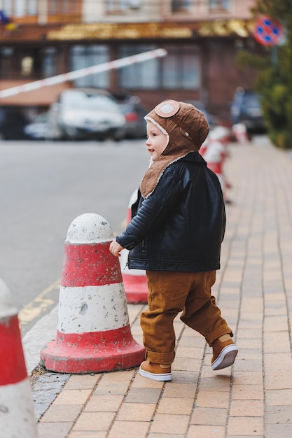 Menino elegante de 3 anos em uma jaqueta de couro e calça marrom anda na rua Criança moderna Moda infantil Criança feliz