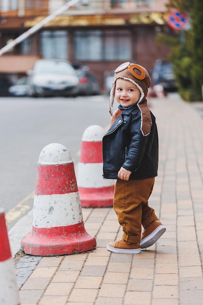 Menino elegante de 3 anos em uma jaqueta de couro e calça marrom anda na rua Criança moderna Moda infantil Criança feliz