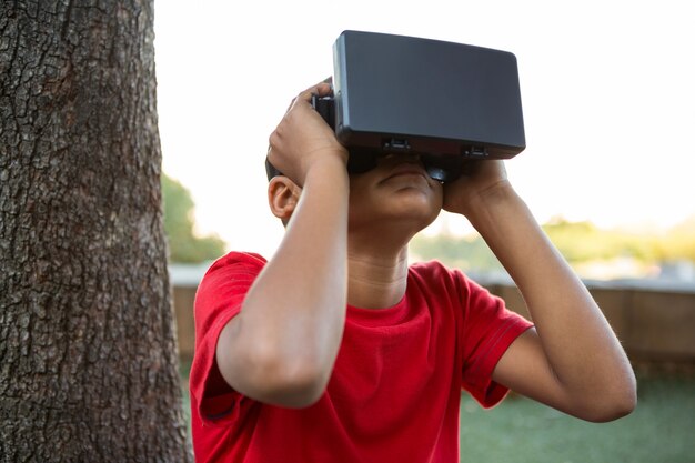 Menino elementar usando fone de ouvido de realidade virtual no parque