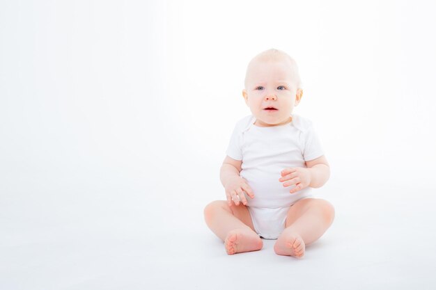 Menino em bodysuit branco sentado em um fundo branco